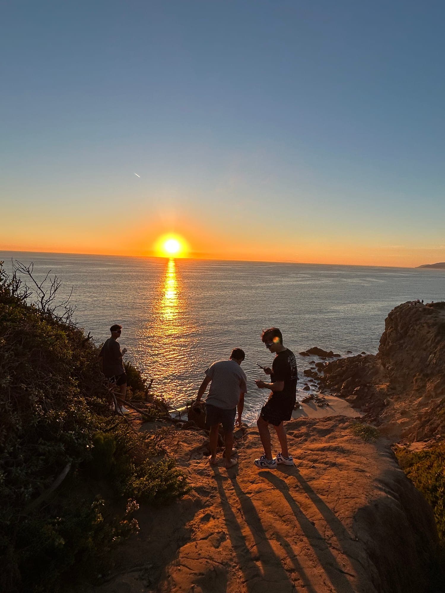 Two people on coastal rocks watching the sun set over the ocean